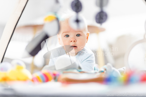 Image of Cute baby boy playing with hanging toys arch on mat at home Baby activity and play center for early infant development. Baby playing at home