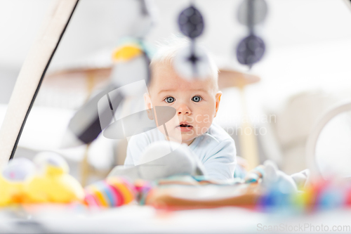 Image of Cute baby boy playing with hanging toys arch on mat at home Baby activity and play center for early infant development. Baby playing at home