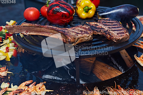 Image of Tomahawk rib beef steak and T-bone on hot black grill.