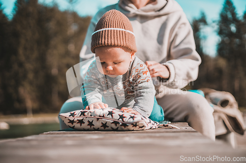 Image of Happy family. Young mother playing with her baby boy infant oudoors on sunny autumn day. Portrait of mom and little son on wooden platform by lake. Positive human emotions, feelings, joy.