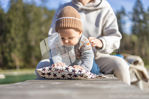 Image of Happy family. Young mother playing with her baby boy infant oudoors on sunny autumn day. Portrait of mom and little son on wooden platform by lake. Positive human emotions, feelings, joy.