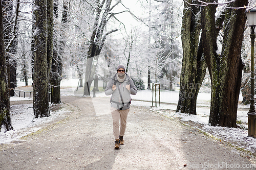 Image of Sporty father carrying his infant son wearing winter jumpsuit and cap in backpack carrier walking in city park in winter