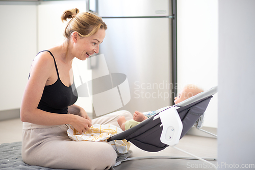 Image of Happy smiling mother playing with her little baby son sitting in electric rocking chair at home. Child development and happy parenting.