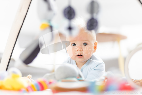Image of Cute baby boy playing with hanging toys arch on mat at home Baby activity and play center for early infant development. Baby playing at home