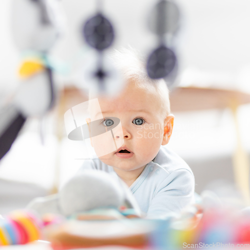 Image of Cute baby boy playing with hanging toys arch on mat at home Baby activity and play center for early infant development. Baby playing at home