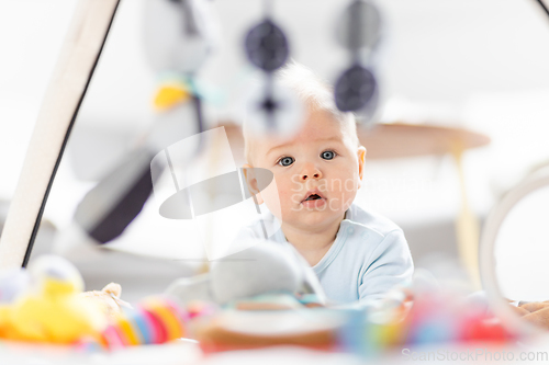 Image of Cute baby boy playing with hanging toys arch on mat at home Baby activity and play center for early infant development. Baby playing at home