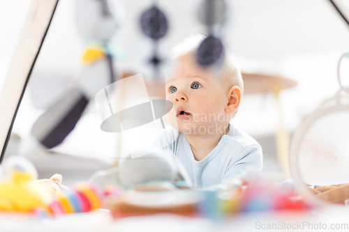 Image of Cute baby boy playing with hanging toys arch on mat at home Baby activity and play center for early infant development. Baby playing at home