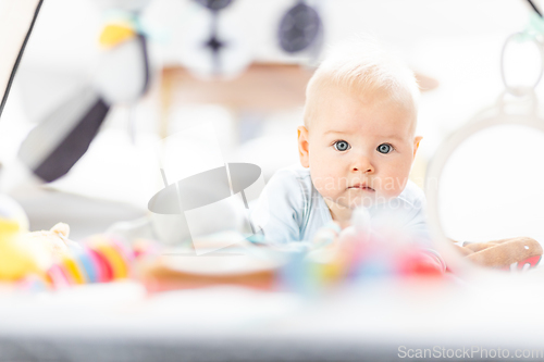 Image of Cute baby boy playing with hanging toys arch on mat at home Baby activity and play center for early infant development. Baby playing at home