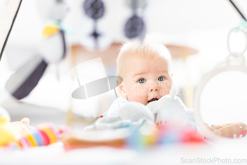 Image of Cute baby boy playing with hanging toys arch on mat at home Baby activity and play center for early infant development. Baby playing at home