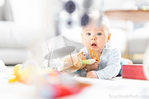 Image of Cute baby boy playing with hanging toys arch on mat at home Baby activity and play center for early infant development. Baby playing at home