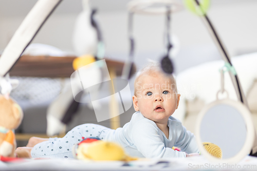 Image of Cute baby boy playing with hanging toys arch on mat at home Baby activity and play center for early infant development. Baby playing at home