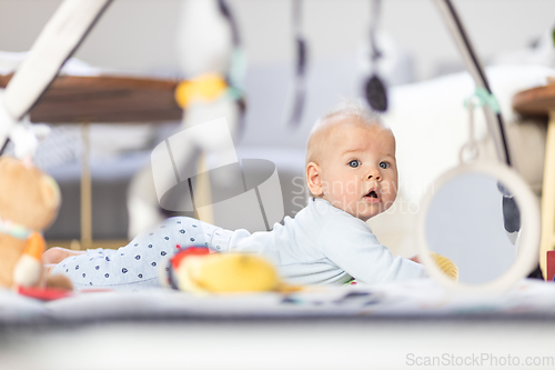 Image of Cute baby boy playing with hanging toys arch on mat at home Baby activity and play center for early infant development. Baby playing at home