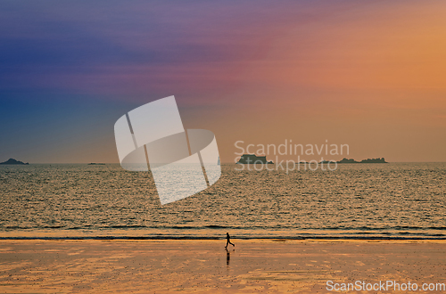 Image of Athlete runs along the sandy shore of the ocean at sunset