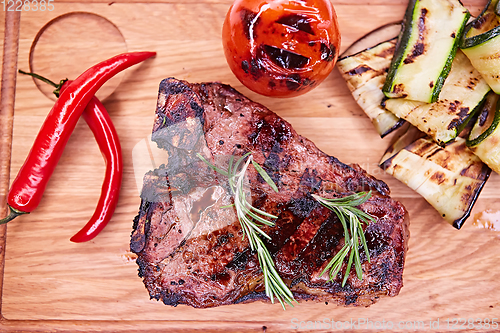 Image of Grilled T-Bone Steak on serving board on wooden background