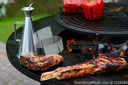 Image of Tomahawk rib beef steak and T-bone on hot black grill.