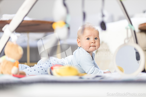 Image of Cute baby boy playing with hanging toys arch on mat at home Baby activity and play center for early infant development. Baby playing at home