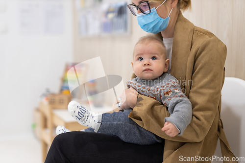 Image of Mother holding infant baby boy in her lap, sitting and waiting in front of doctor's office for pediatric well check. child's health care concept