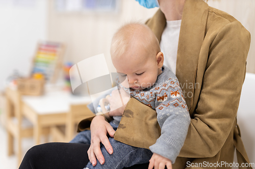 Image of Mother holding infant baby boy in her lap, sitting and waiting in front of doctor's office for pediatric well check. child's health care concept