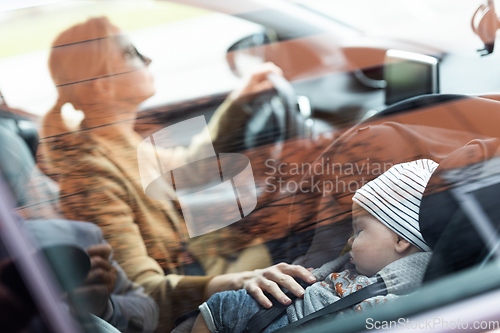 Image of Mother concentrating on driving family car running errands while her baby sleeps in infant car seat by her site.