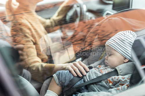 Image of Mother concentrating on driving family car running errands while her baby sleeps in infant car seat by her site.