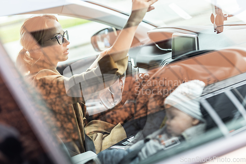 Image of Mother concentrating on driving family car running errands while her baby sleeps in infant car seat by her site.