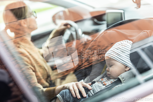 Image of Mother concentrating on driving family car running errands while her baby sleeps in infant car seat by her site.