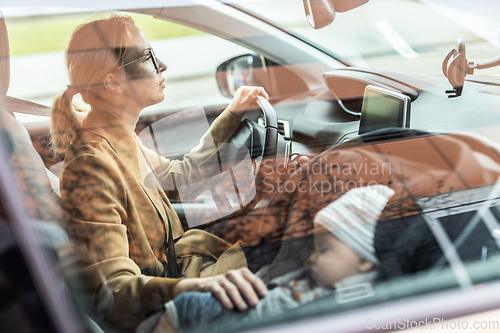 Image of Mother concentrating on driving family car running errands while her baby sleeps in infant car seat by her site.