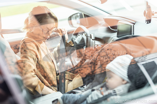 Image of Mother fastening seat belt, driving family car, running errands while her baby sleeps in infant car seat by her site.