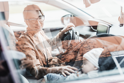 Image of Mother concentrating on driving family car running errands while her baby sleeps in infant car seat by her site.