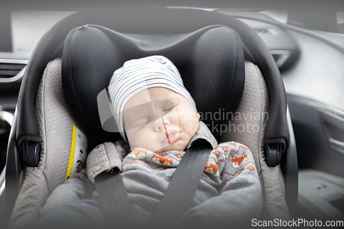 Image of Cute little baby boy sleeping strapped into infant car seat in passenger compartment during car drive.