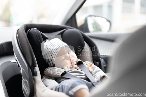 Image of Cute little baby boy sleeping strapped into infant car seat in passenger compartment during car drive.