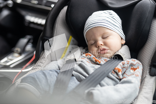 Image of Cute little baby boy sleeping strapped into infant car seat in passenger compartment during car drive.