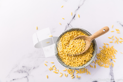 Image of Raw orzo pasta (risoni) in bowl with wooden spoon