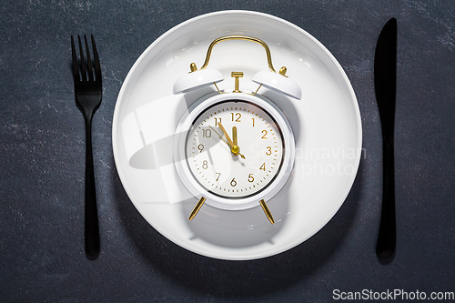 Image of White plate and clock on a dark background with copy space. Concept of interval fasting and autophagy.