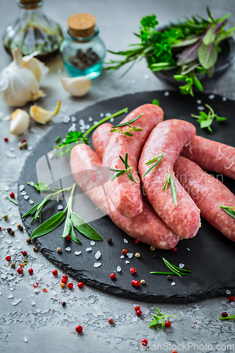 Image of Raw sausages on slate, with herbs and spices, prepared for grill and BBQ