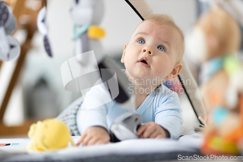 Image of Cute baby boy playing with hanging toys arch on mat at home Baby activity and play center for early infant development. Baby playing at home