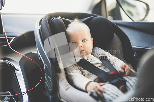 Image of Cute little baby boy strapped into infant car seat in passenger compartment during car drive.