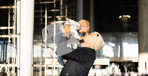 Image of Father happily holding and lifting his infant baby boy child in the air after being rejunited in front of airport terminal station. Baby travel concept.