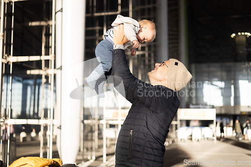 Image of Father happily holding and lifting his infant baby boy child in the air after being rejunited in front of airport terminal station. Baby travel concept.