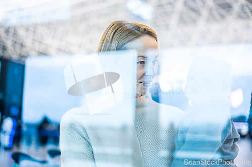 Image of Thoughtful young mother looking trough window holding his infant baby boy child while waiting to board an airplane at airport terminal departure gates. Travel with baby concept.