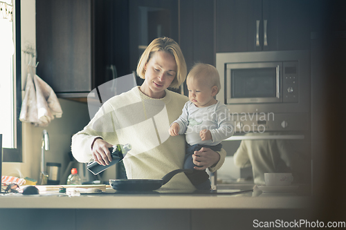 Image of Happy mother and little infant baby boy together making pancakes for breakfast in domestic kitchen. Family, lifestyle, domestic life, food, healthy eating and people concept.