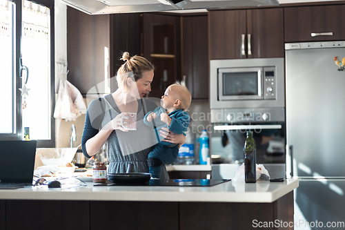 Image of Happy mother and little infant baby boy together making pancakes for breakfast in domestic kitchen. Family, lifestyle, domestic life, food, healthy eating and people concept.