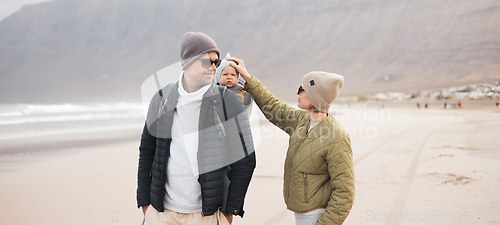 Image of Young father carrying his infant baby boy son in backpack on windy sandy beach. Family travel and winter vacation concept.