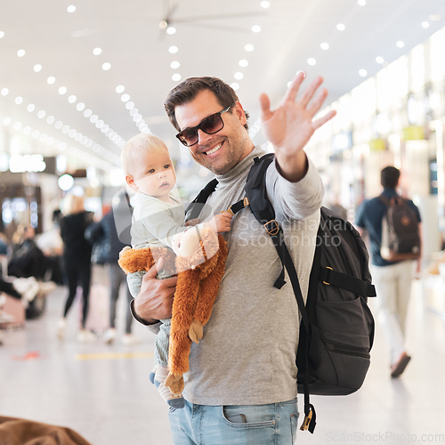 Image of Father traveling with child, holding his infant baby boy at airport terminal waiting to board a plane waving goodby. Travel with kids concept.