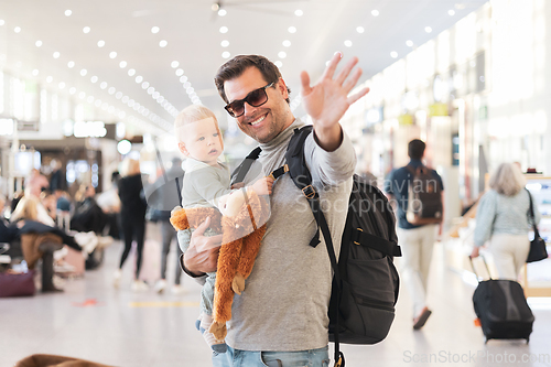 Image of Father traveling with child, holding his infant baby boy at airport terminal waiting to board a plane waving goodby. Travel with kids concept.