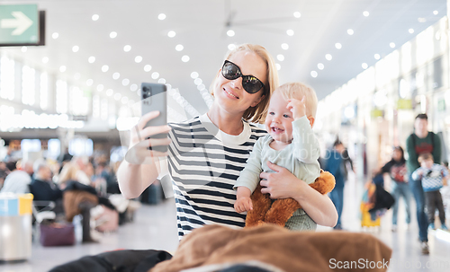 Image of Mother taking selfie with mobile phone, while traveling with child, holding his infant baby boy at airport, waiting to board a plane. Travel with kids concept.