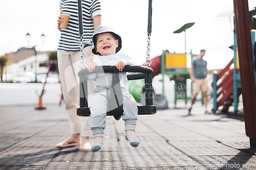 Image of Mother pushing her infant baby boy child on a swing on playground outdoors.