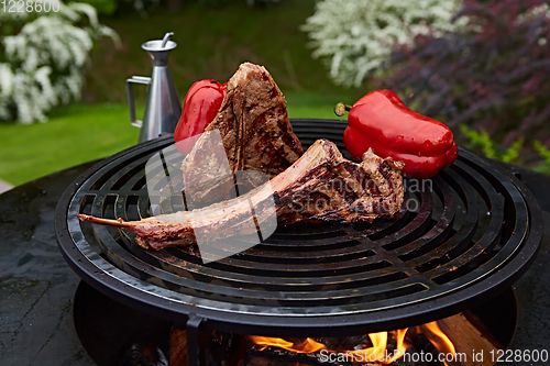 Image of Tomahawk rib beef steak and T-bone on hot black grill.