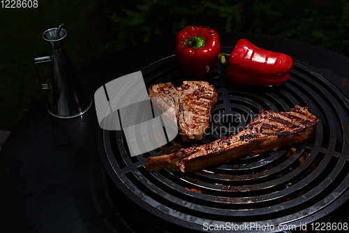 Image of Tomahawk rib beef steak and T-bone on hot black grill.