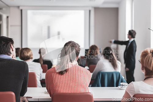 Image of Speaker giving presentation in lecture hall at university. Participants listening to lecture and making notes